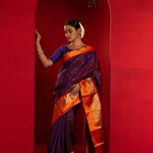 A woman gracefully poses in a vibrant Indian saree with a red background, showcasing traditional fashion.